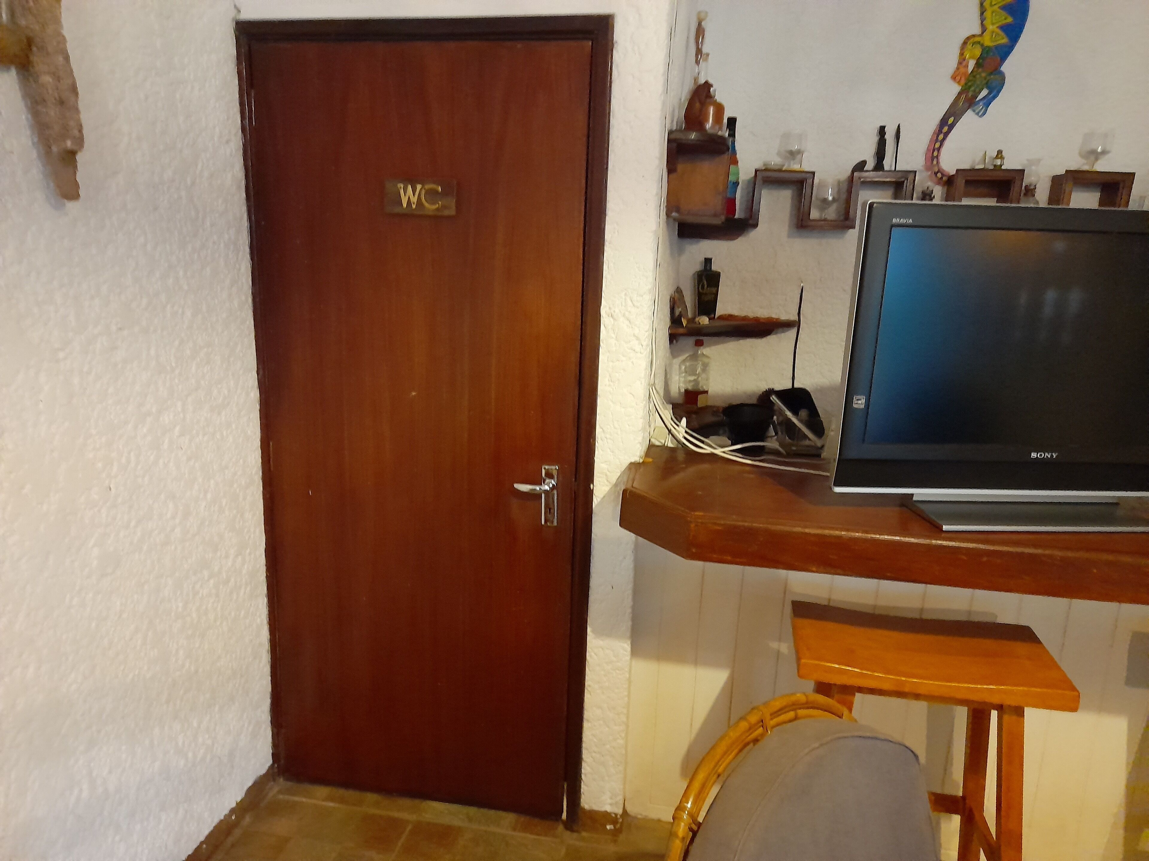 Une porte en bois avec une pancarte indiquant les toilettes, une table en bois avec un ordinateur portable et une petite étagère contenant divers objets.