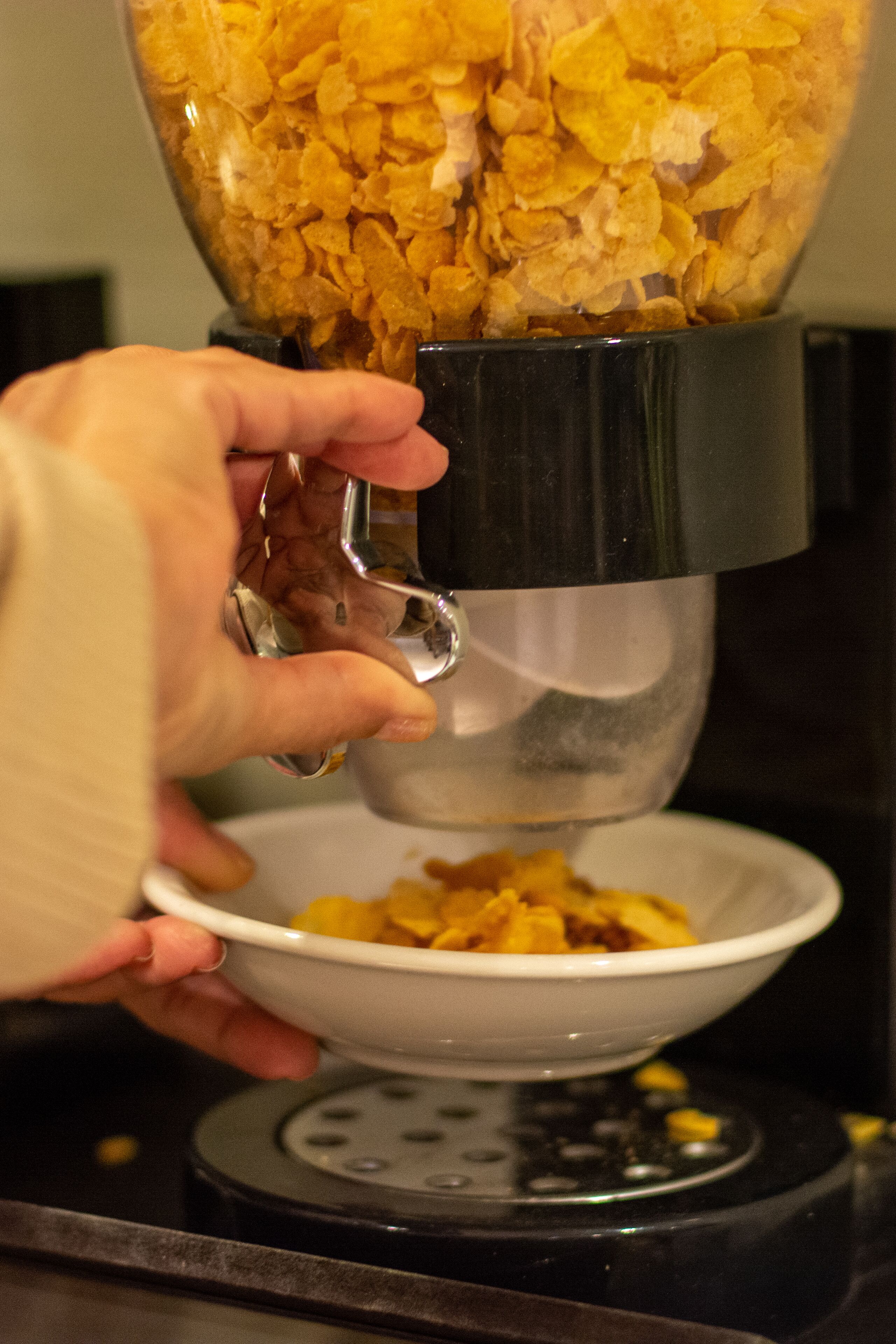 Una mano usa una cuchara metálica para pasar copos de cereal desde una licuadora a un tazón.