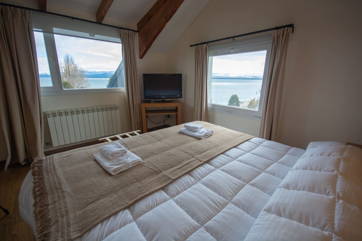 Quarto com cama, televisão em suporte e vista para o mar.