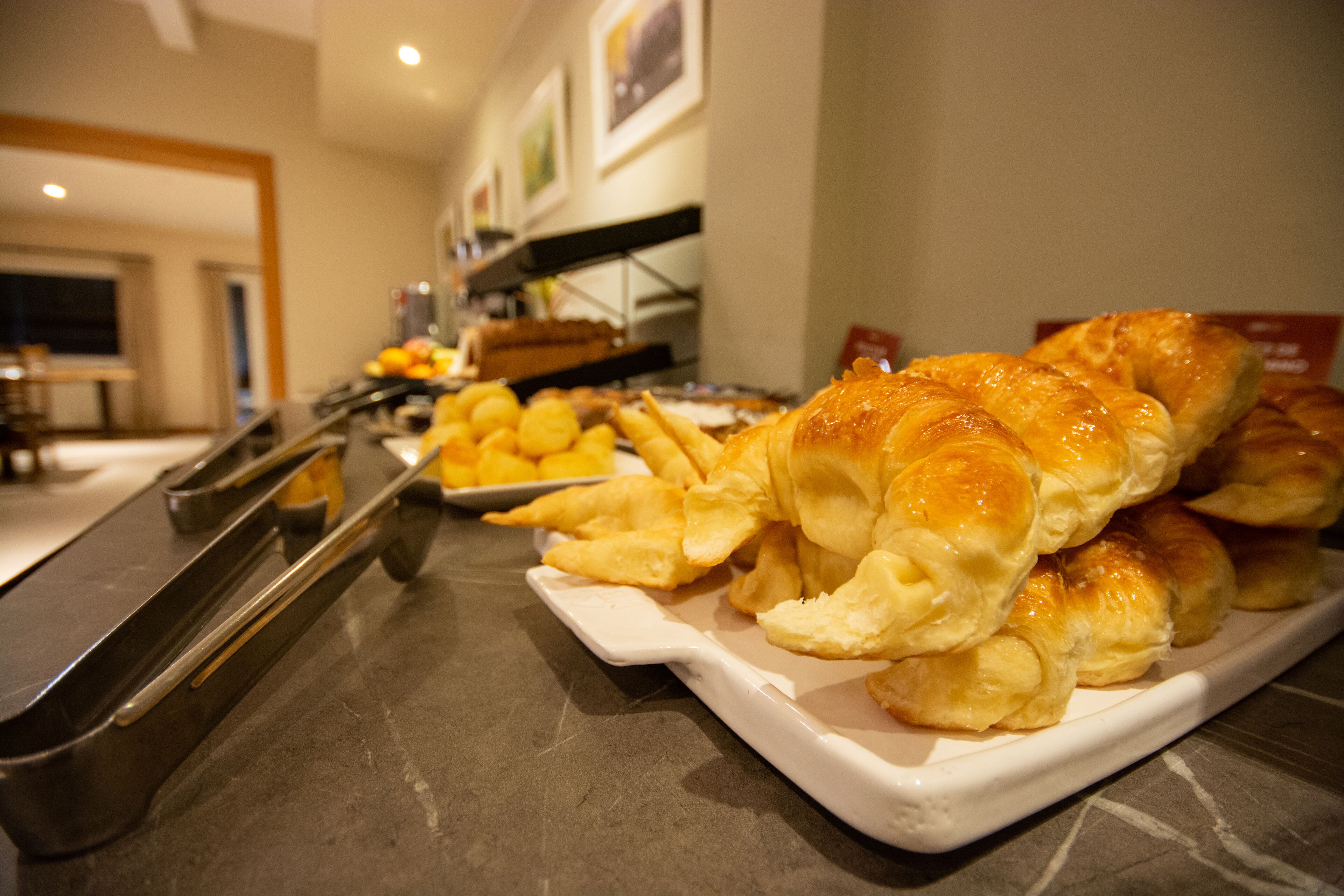 Una mesa de buffet con diversas opciones de panadería, incluyendo croissants y pasteles, en un entorno hotelero.