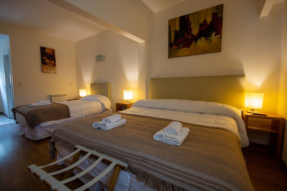 Quarto de hotel com duas camas, cada uma com cabeceira, mesas de cabeceira, luminárias e toalhas dobradas com capricho.