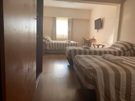 Quarto de hotel com duas camas, uma escrivaninha, uma cadeira e televisão na parede.
