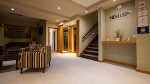 Un hall d’hôtel avec des fauteuils à rayures, un comptoir d’accueil, un escalier et une enseigne murale indiquant « NATHIVO BOUTIQUE HOTEL ».