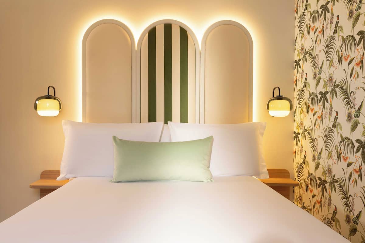Una habitación de hotel con una cama, dos lámparas de noche y un papel tapiz floral.