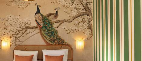 A room with a bed, pillows, a peacock mural, wall sconces, and a striped wall.