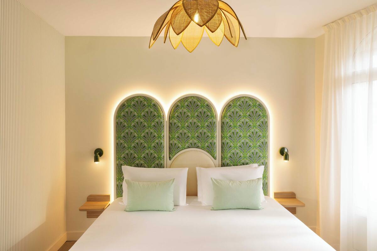 Un dormitorio con una cama grande, una lámpara decorativa en el techo y un papel tapiz estampado.