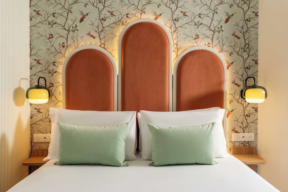 Una cama con cabecera, dos lámparas de noche y una pared con estampado floral.