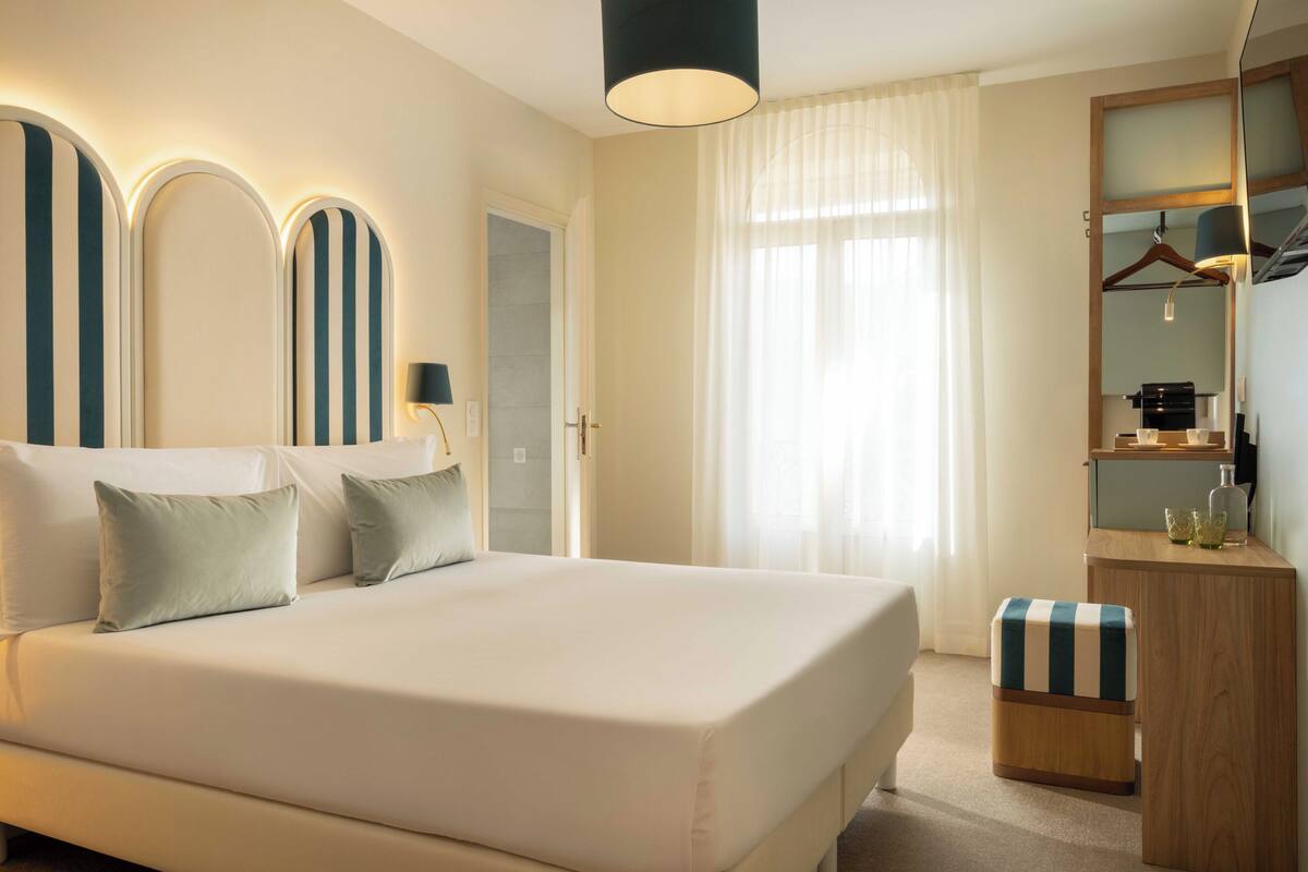 Una habitación de hotel con una cama grande, mesitas de noche, un espejo y un armario.