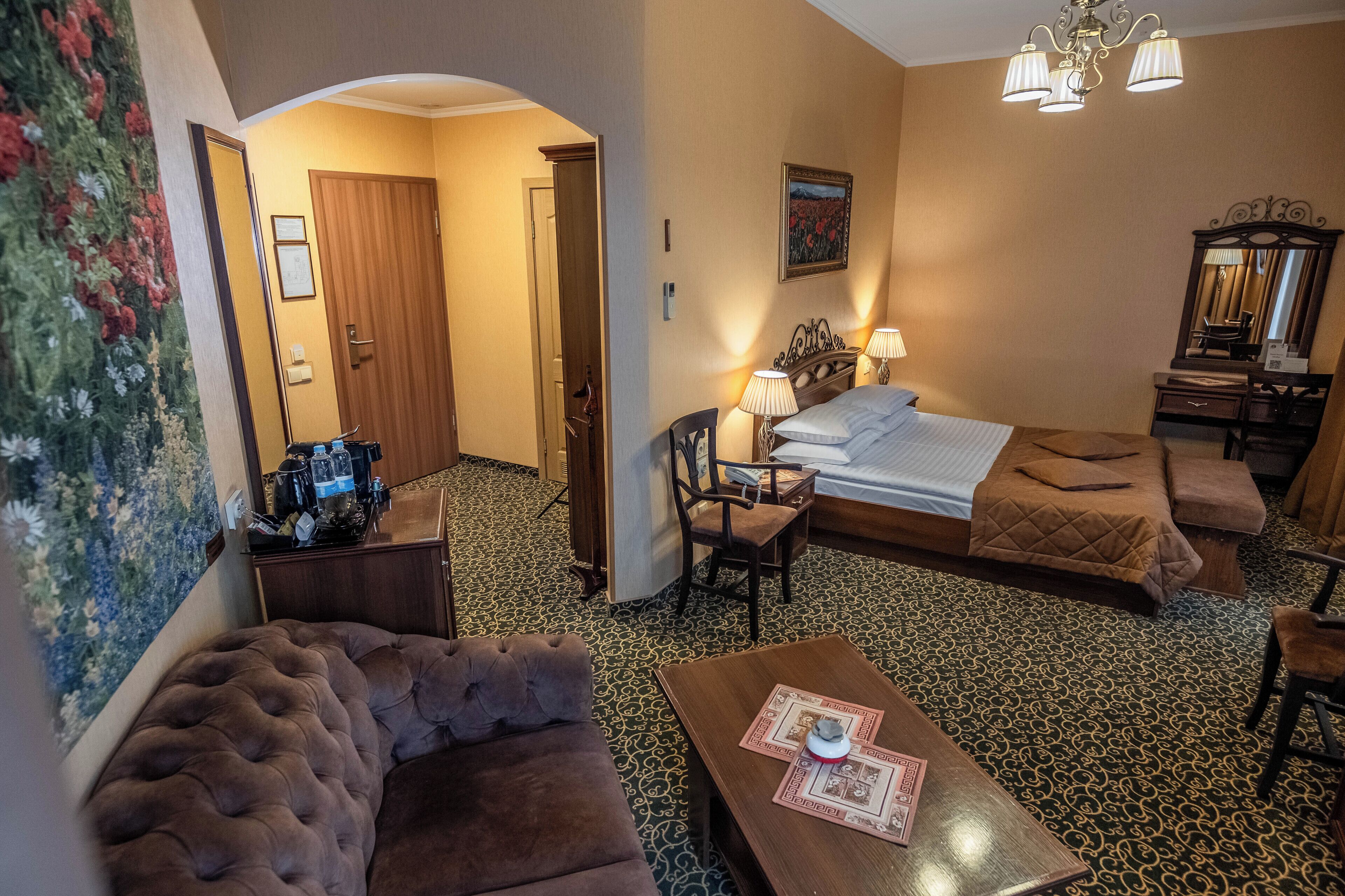 A hotel room with a bed, a sofa, a table, a chair, a desk, and a mirror.