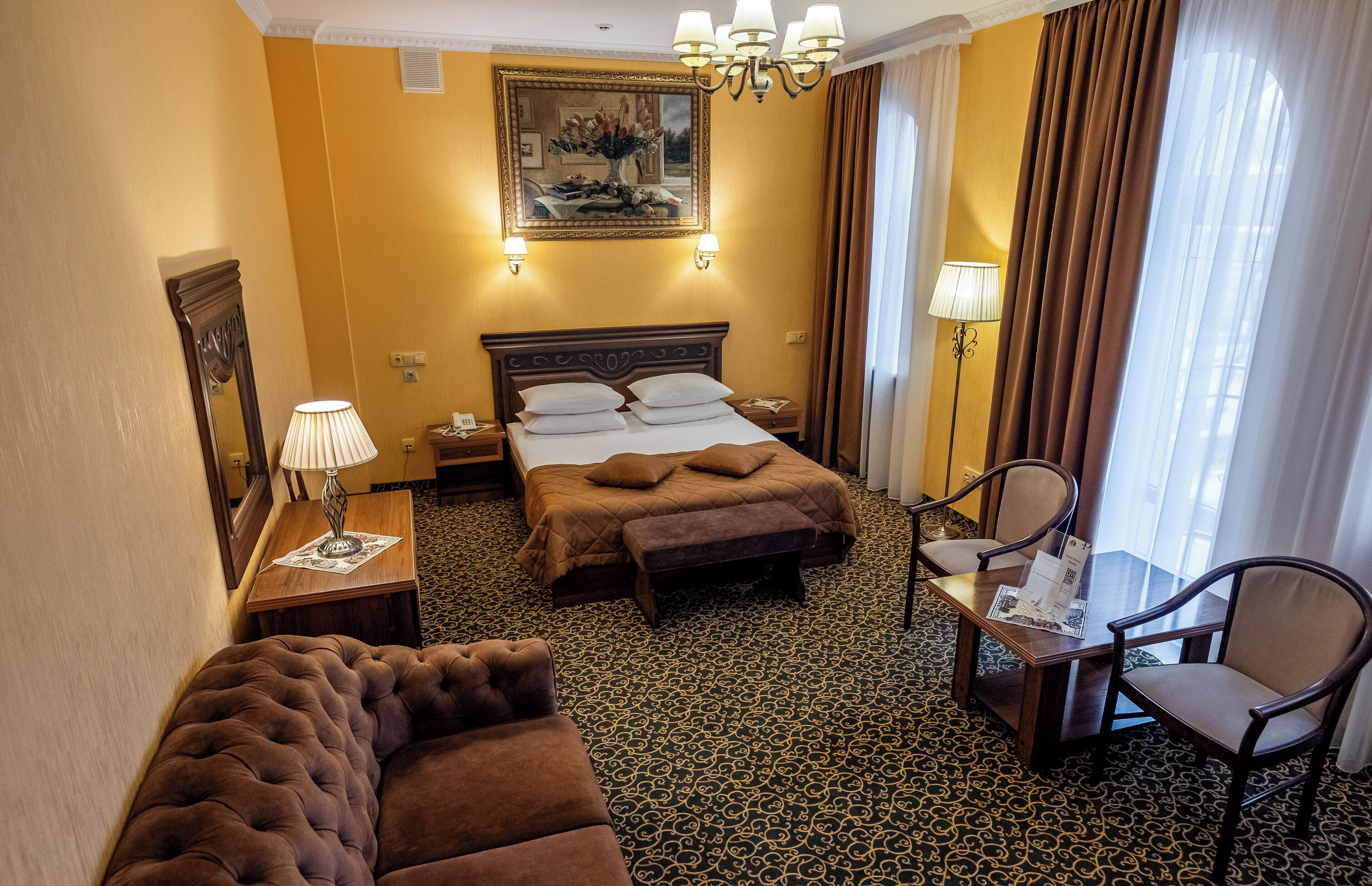 Habitación de hotel con una cama grande, una zona de estar con sofá y sillones, una mesita y un escritorio con lámpara.