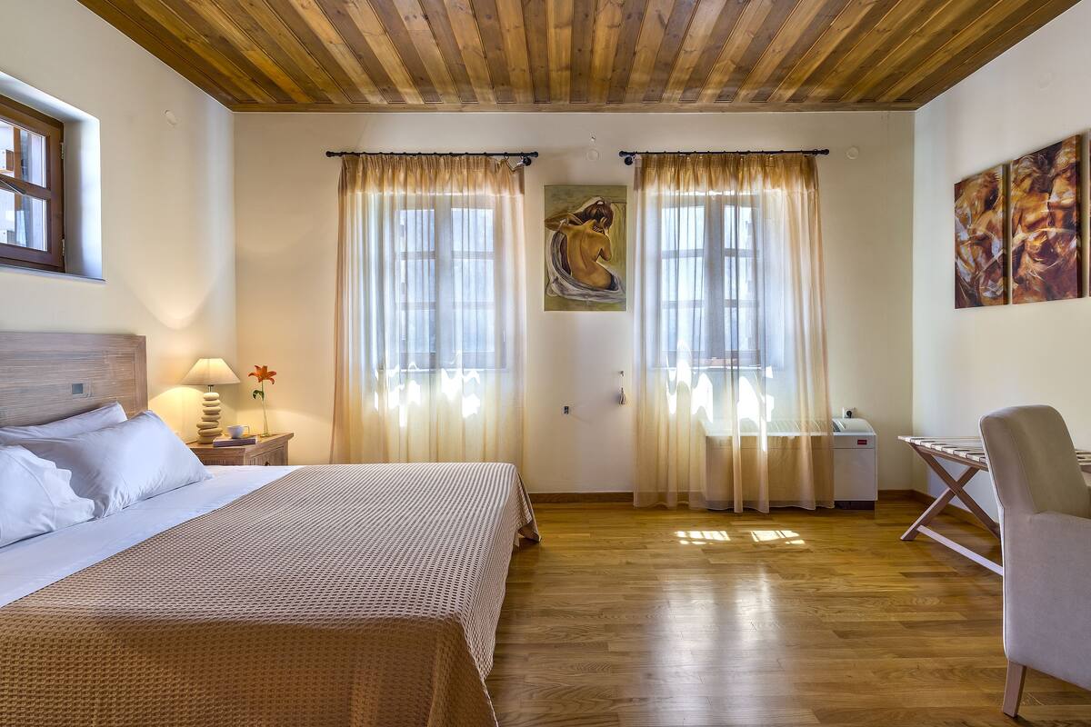 A bedroom with a bed, a desk, and a chair. There are curtains on the windows, and a painting on the wall.