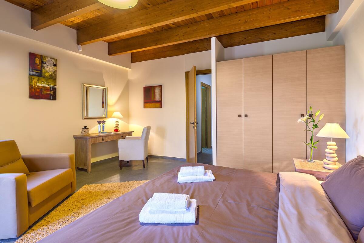 A bedroom with a large bed, a desk, a chair, a wardrobe, and a bathroom visible through an open door.