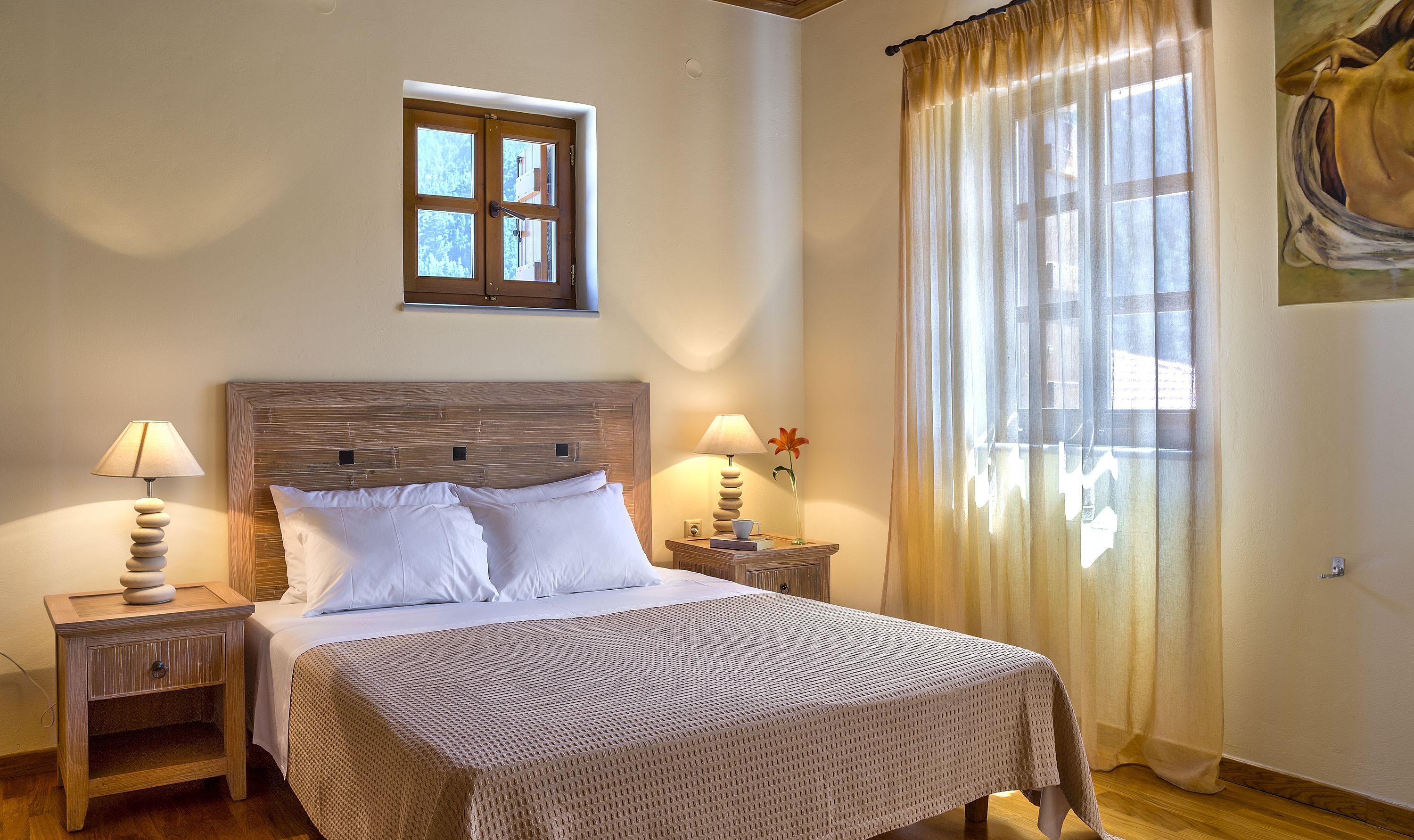 A bedroom with a large bed, two bedside tables, a window with curtains, and a painting on the wall.