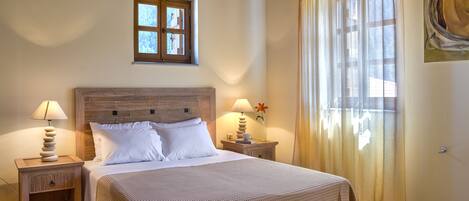 A bedroom with a large bed, two bedside tables, a window with curtains, and a painting on the wall.