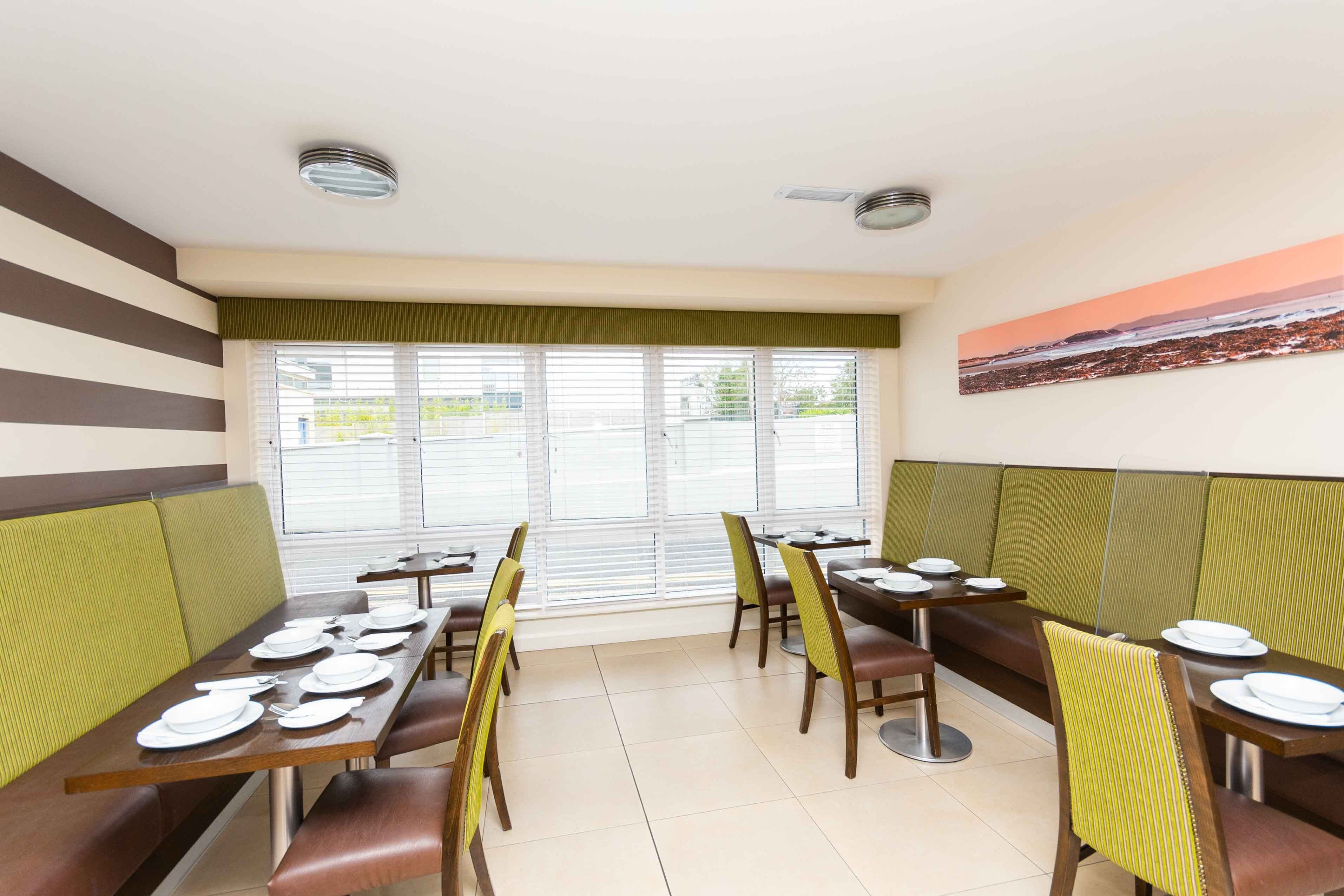 A dining area with booths and tables, green cushioned seating, and a cityscape painting on the wall.