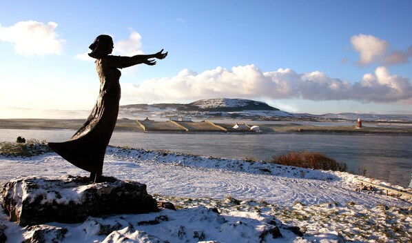 A statue of a woman in a long dress standing on a rock with a snowy landscape and a river in the background. - Strandhill Boutique Hotel (Strandhill)
