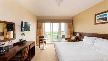 A hotel room with a large bed, a desk with a computer and phone, a chair, a TV, and a window with curtains.