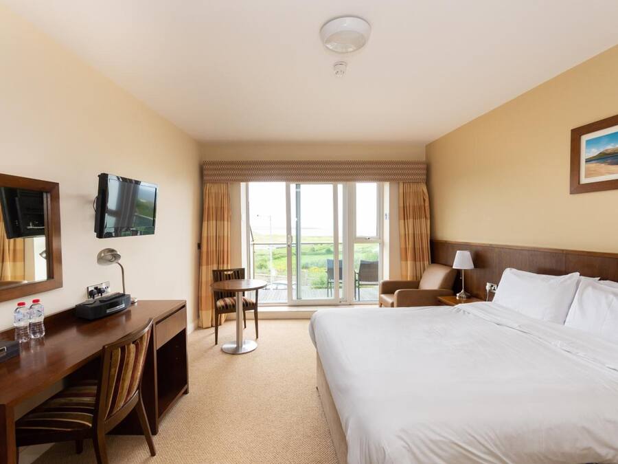 A hotel room with a large bed, a desk with a computer and phone, a chair, a TV, and a window with curtains.