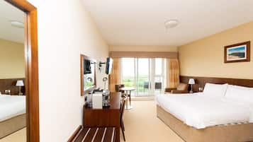Une chambre d’hôtel avec un grand lit, un bureau avec une chaise, une petite table et une fenêtre donnant sur un paysage verdoyant.
