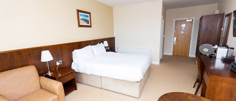 A hotel room with a bed, a wooden nightstand, a lamp, a wooden chair, a desk, and a mirror.