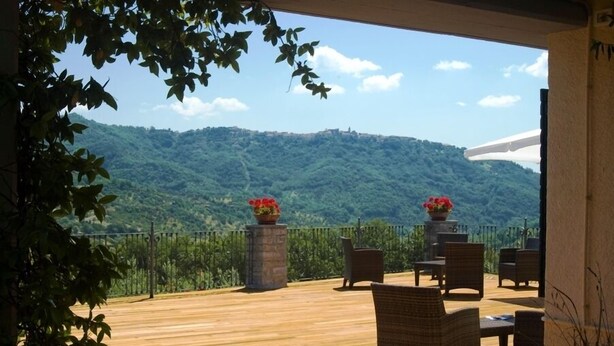A wooden deck with wicker furniture and flower planters, overlooking a lush green hillside. - Masseria Santa Lucia (Agnone)