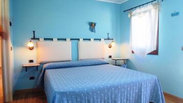 Un dormitorio con cama, dos mesitas de noche, una lámpara auxiliar y una ventana con cortina, además de luces fijadas a la pared.