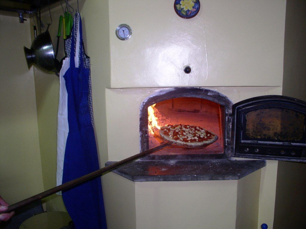 Un horno de pizza con una pizza adentro, un reloj y un mandil azul colgado cerca.