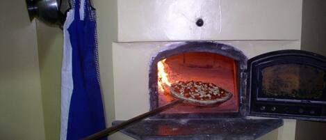 Un horno de pizza con una pizza adentro, un reloj y un mandil azul colgado cerca.
