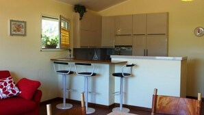 A compact kitchen with a bar area, three bar stools, and a red sofa. - Masseria Santa Lucia (Agnone)