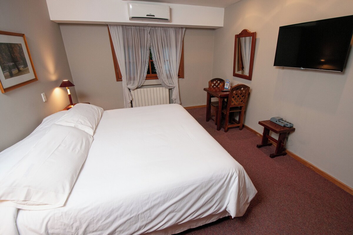 Ein Hotelzimmer mit einem großen Bett, einem Schreibtisch, einem Sessel, einem Fernseher und einer Klimaanlage.