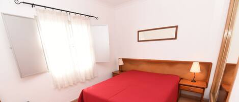 Un dormitorio con una cama, una mesita de noche, una silla, una ventana con cortinas y un cuadro colgado en la pared.
