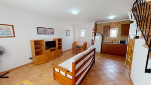 A compact living space with a TV, seating area, kitchenette, and a staircase. - Monte dos Avós Village - Pets Friendly (Tavira)