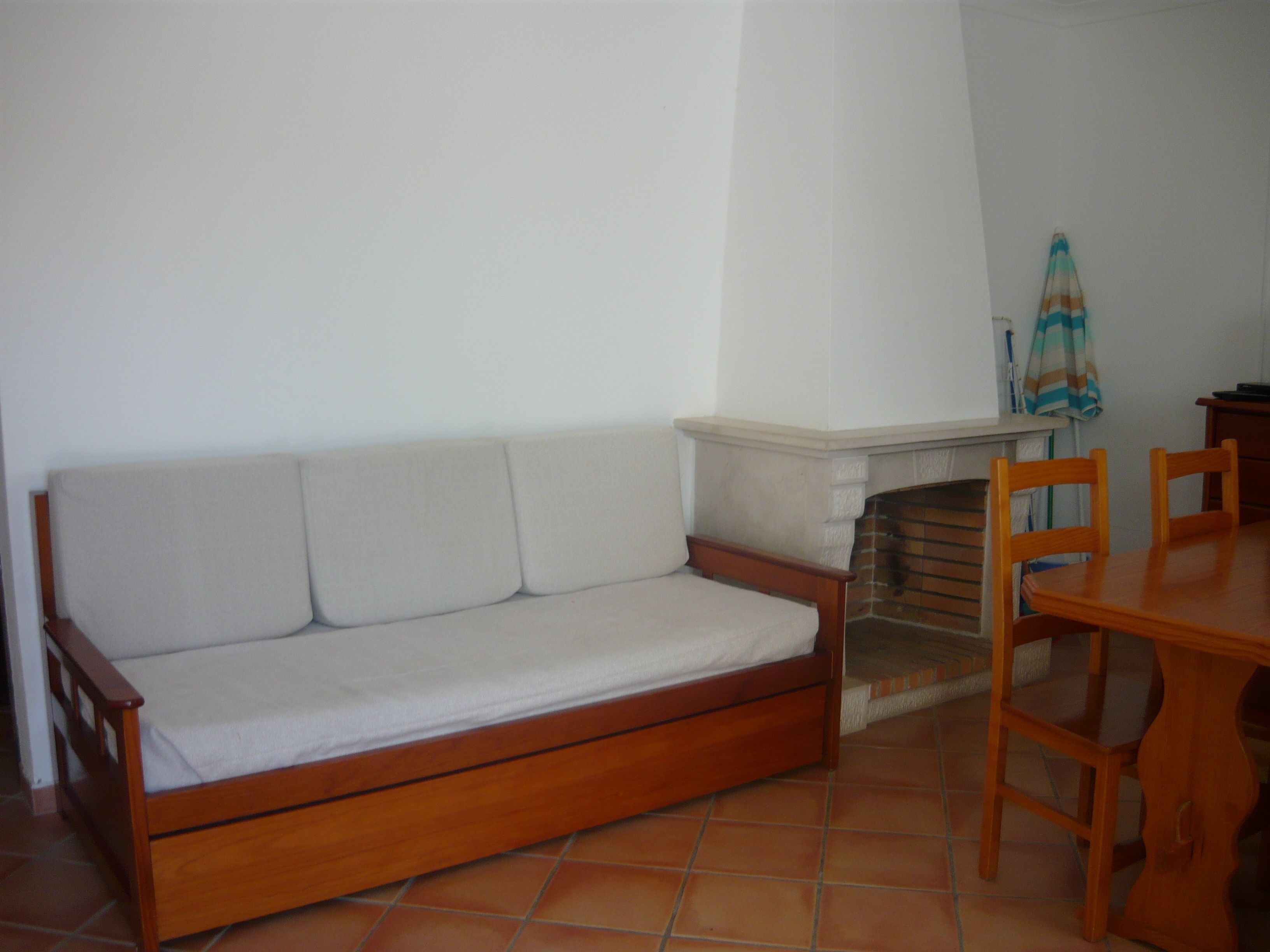 Un sofá de madera con cojines, suelo de baldosas, chimenea y una mesa de madera con sillas.