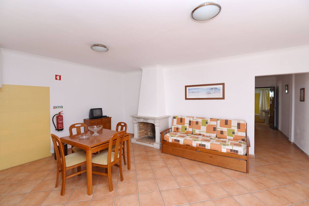 A room with a dining table, chairs, a sofa, a fireplace, and a television.