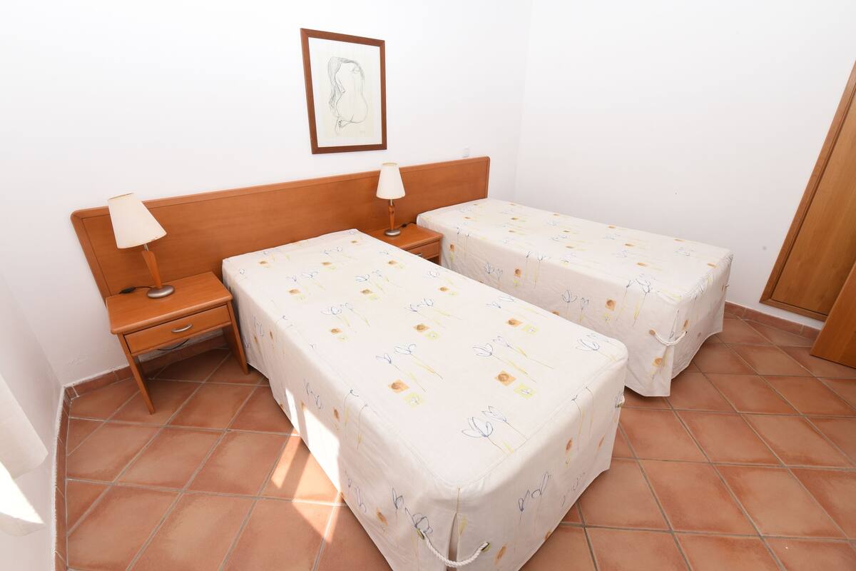 A room with two beds, a nightstand, a lamp, and a framed picture on the wall.