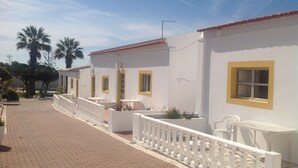 A building with white walls and yellow window frames, a paved walkway, and a white railing. - Monte dos Avós Village - Pets Friendly (Tavira)