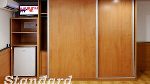 Ein Standardzimmer mit Kleiderschrank, kleinem Kühlschrank und Wandfernseher.