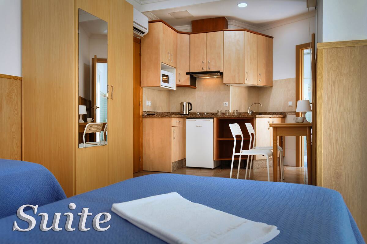 A hotel suite with a bed, a kitchenette, and a small dining area.