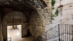 An arched stone passageway with a metal railing, leading to an open area with tiled flooring. - Villa Marta (Split)