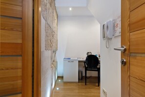 A narrow hallway with a wooden door on the left, a white desk with a chair and a telephone on the right, and a stone wall. - Villa Marta (Split)