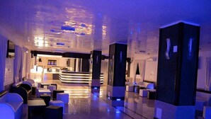Een moderne hotellobby met een centraal gelegen receptiebalie, zithoeken en een zichtbare keuken op de achtergrond.