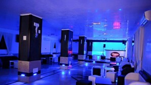 Een moderne hotellobby met een blauwe sfeerverlichting, met een receptiebalie, zithoeken en een zichtbaar 'CINNABON' bord.