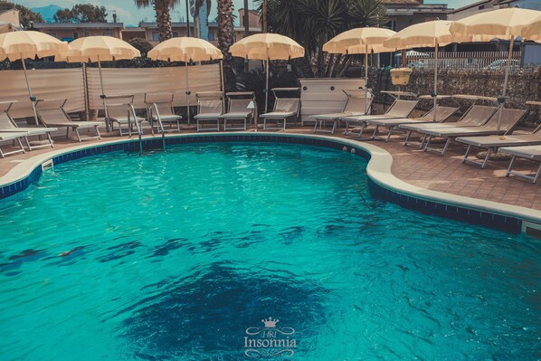 Een buitenzwembad, parasols bij het zwembad en ligstoelen