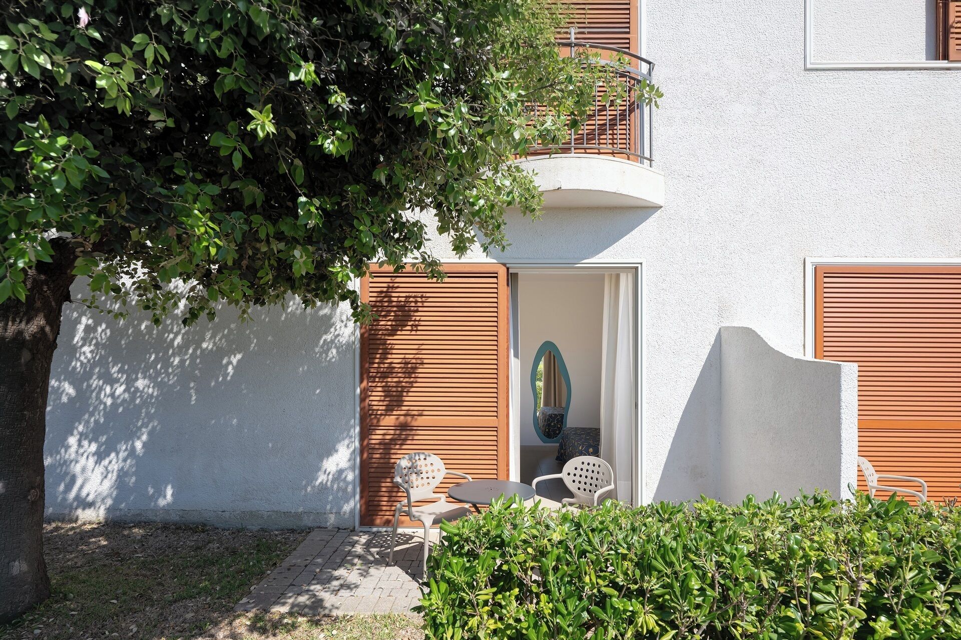 A building with a white exterior, wooden shutters, and a small patio area with outdoor furniture.