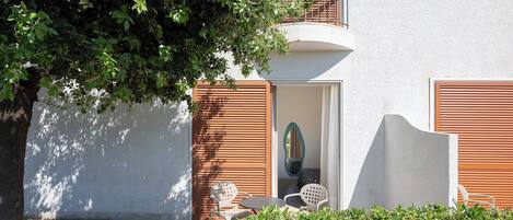 Un edificio con fachada blanca, contraventanas de madera y un pequeño patio con mobiliario exterior.