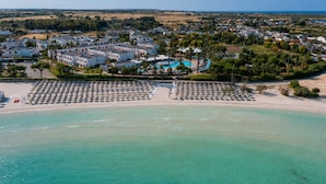 An aerial view of a coastal resort with a beach, a swimming pool, and a cluster of white buildings. - Blu Salento Village (Nardò)