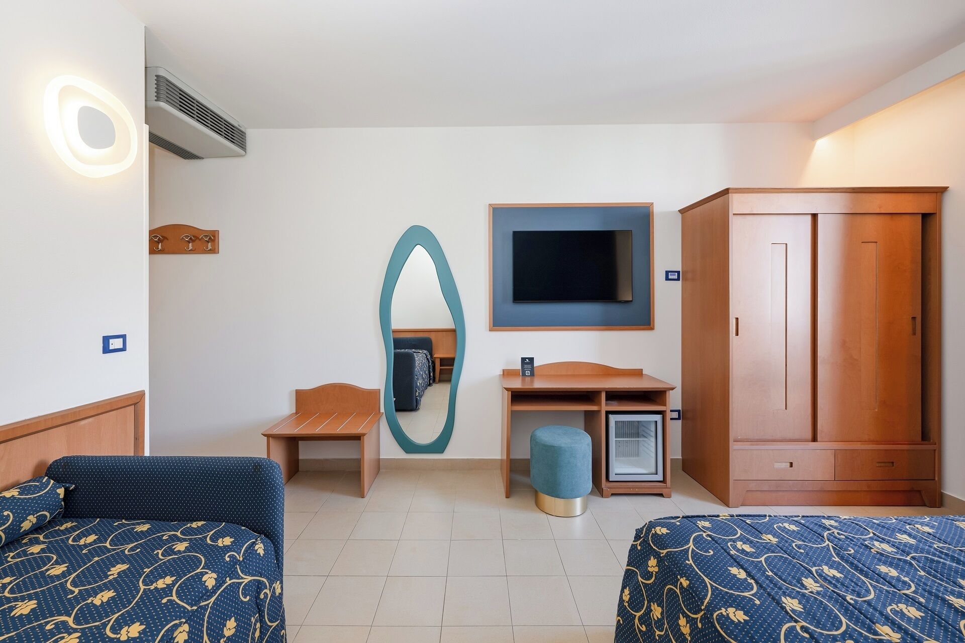 Habitación de hotel con dos camas, televisión, espejo, escritorio y armario.