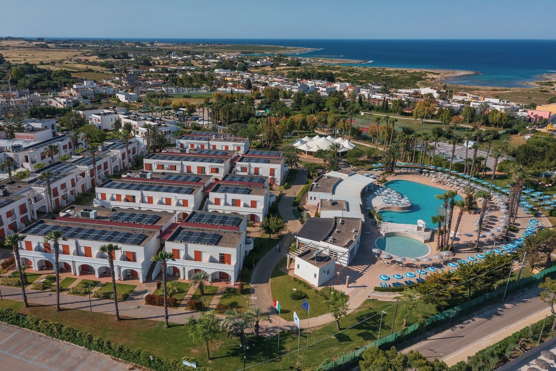 A resort with multiple buildings, a swimming pool, and a view of the sea.