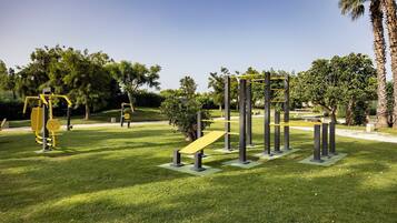 Una palestra all'aperto con diverse attrezzature per esercizi, immersa nel verde tra l'erba e gli alberi.