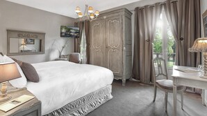 A bedroom with a large bed, a wardrobe, a desk with a lamp, and a chair.